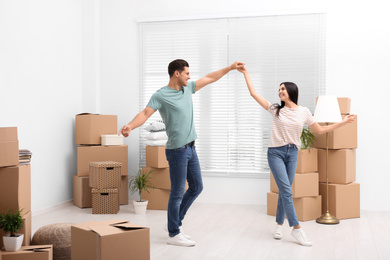 Happy couple dancing in room with cardboard boxes on moving day