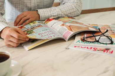 Photo of Man reading culinary magazine at white marble table, closeup