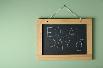 Photo of Blackboard with words Equal Pay and gender symbols hanging on light green wall. Space for text