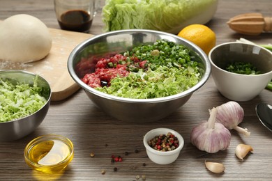 Bowl with gyoza filling, raw dough and ingredients on wooden table