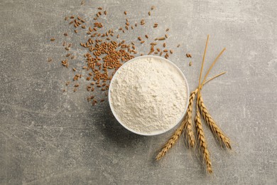 Bowl of flour, wheat ears and kernels on light grey table, flat lay