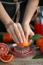Woman squeezing sicilian orange juice at wooden table, closeup