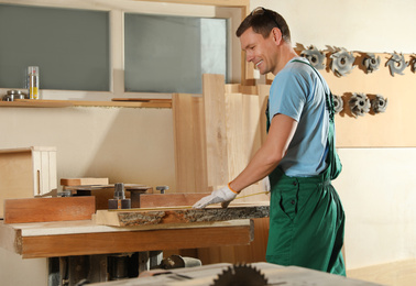 Professional carpenter measuring wooden board in workshop