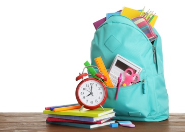 Stylish schoolbag with different stationary and alarm clock on wooden table, white background