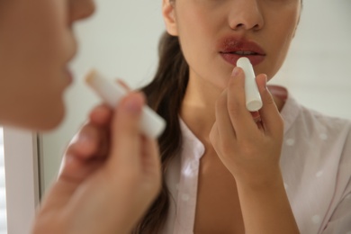 Woman with herpes applying lip balm in front of mirror, closeup
