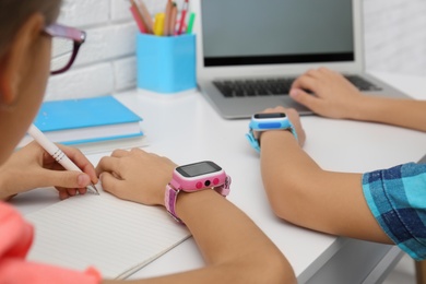 Children with stylish smart watches at white table, closeup