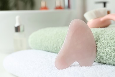 Photo of Rose quartz gua sha tool with towels on white countertop in bathroom, closeup. Space for text
