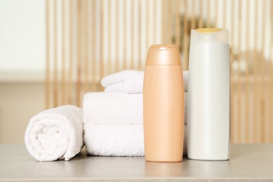 Photo of Soft folded terry towels and cosmetic bottles on light gray table indoors