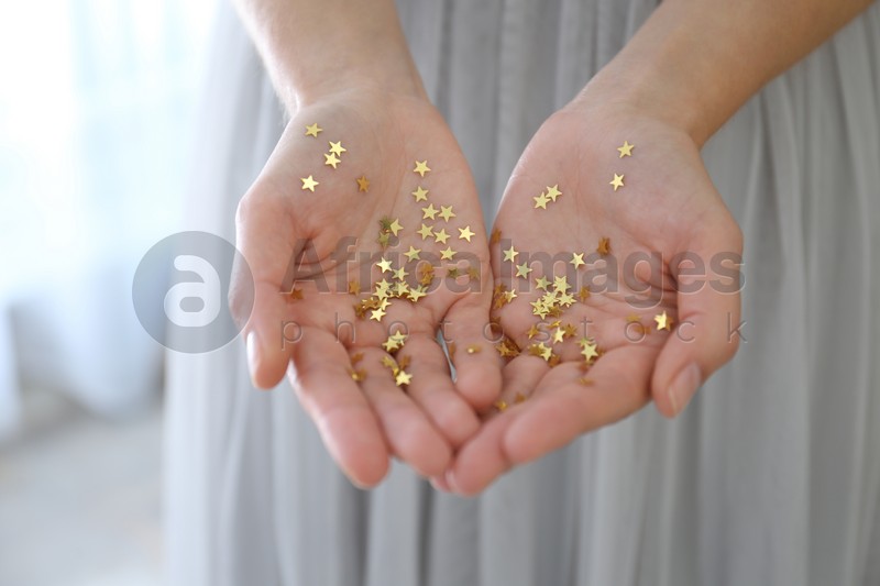 Woman holding gold confetti stars at home, closeup. Christmas celebration