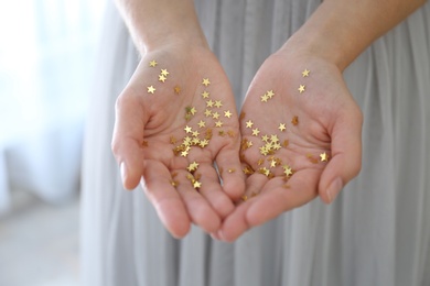 Woman holding gold confetti stars at home, closeup. Christmas celebration