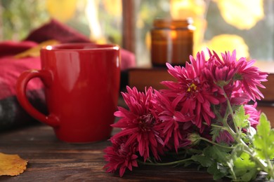 Beautiful chrysanthemum flowers and cup of hot drink on wooden table, closeup. Autumn still life