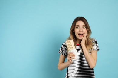 Photo of Emotional young woman with delicious shawarma on turquoise background, space for text