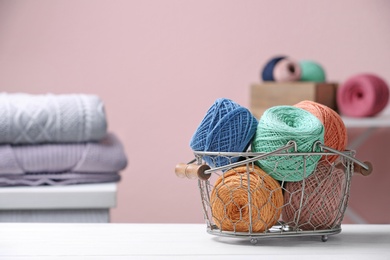 Colorful clews of threads in basket on table against blurred background, space for text