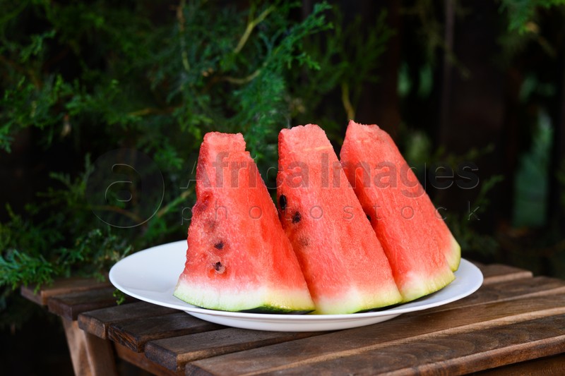 White plate with sliced watermelon on wooden stool outdoors