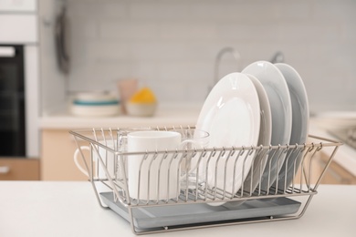 Dish drainer with clean dinnerware on table in kitchen