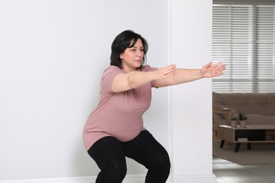 Overweight mature woman squatting near wall at home