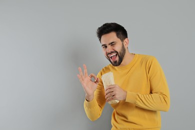 Photo of Happy young man with tasty shawarma showing okay gesture on grey background. Space for text