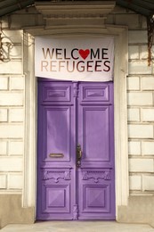 Banner with phrase WELCOME REFUGEES hanging on closed vintage wooden door