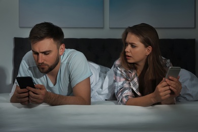 Photo of Upset young couple with smartphones in bed at nighttime