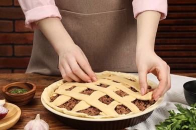 Photo of Woman making lattice top for meat pie at wooden table, closeup
