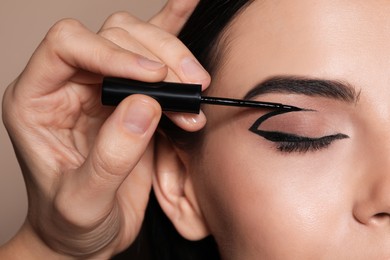 Photo of Artist applying black eyeliner onto woman's face on beige background, closeup