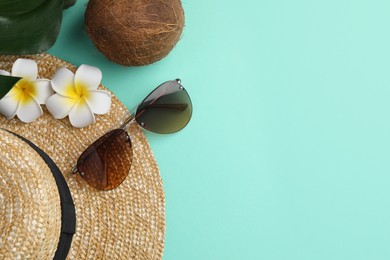 Stylish sunglasses, straw hat, coconut and beautiful plumeria flowers on turquoise background, flat lay. Space for text
