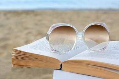 Photo of Open book and sunglasses on beach, closeup