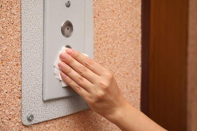 Woman using tissue paper to press elevator call button, closeup