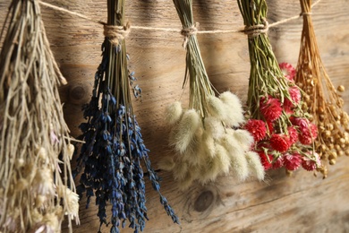 Bunches of beautiful dried flowers hanging on rope near wooden wall, closeup