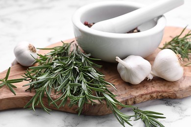Sprigs of rosemary, mortar and garlic on white marble background, closeup