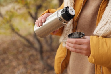 Woman pouring drink from thermos into cap outdoors, closeup