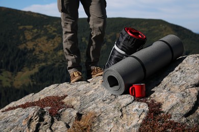 Tourist with sleeping bag, mat and cup on mountain peak, closeup