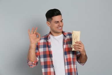 Man with delicious shawarma on grey background