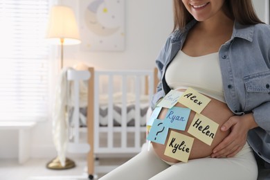 Pregnant woman with different baby names on belly at home, closeup. Space for text