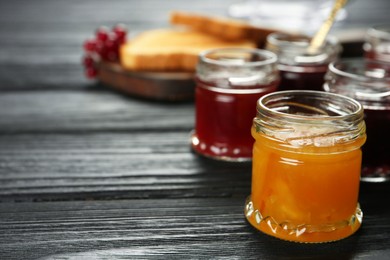 Jars of different jams on black wooden table, space for text