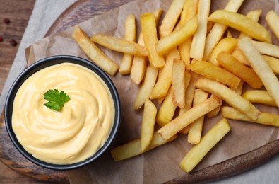 Delicious French fries and cheese sauce with parsley on wooden table, top view
