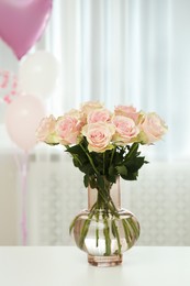 Photo of Beautiful roses in glass vase and balloons on white table indoors. Happy birthday greetings
