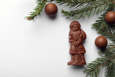 Flat lay composition with chocolate Santa Claus, fir tree twigs and sweets on white background, space for text