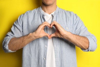 Man making heart with hands on yellow background, closeup