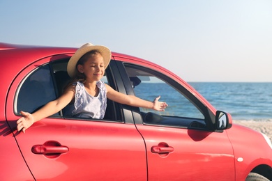 Happy little girl leaning out of car window on beach. Summer trip