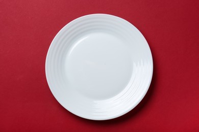 Empty white ceramic plate on red background, top view
