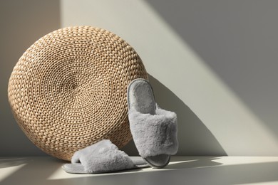 Pair of soft slippers and wicker pouf on floor near white wall, space for text