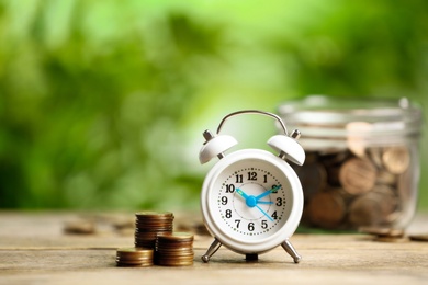 White alarm clock and stacked coins on wooden table against blurred background. Money savings