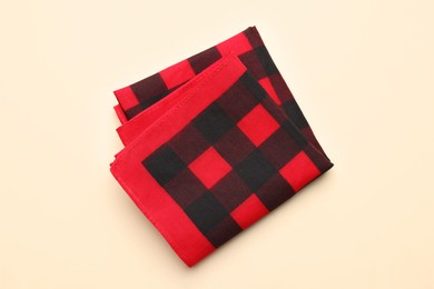 Folded red checkered bandana on beige background, top view