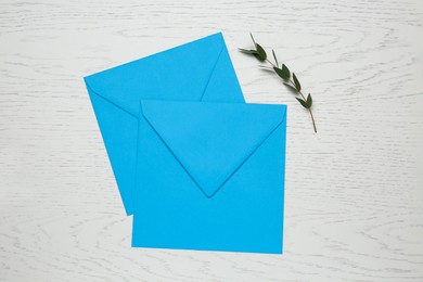 Turquoise envelopes and green twig on white wooden table, flat lay