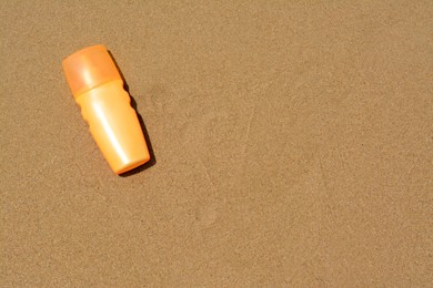 Photo of Bottle with sun protection spray on sandy beach, top view. Space for text
