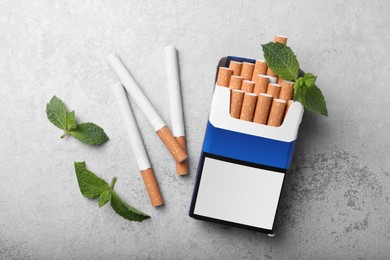 Pack of menthol cigarettes and mint leaves on grey table, flat lay