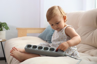 Photo of Cute baby playing with power strip on sofa at home. Dangerous situation