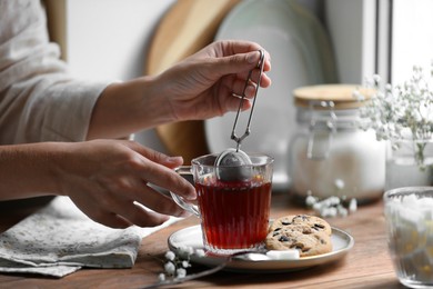 Young woman using snap infuser for brewing tea at wooden table, closeup