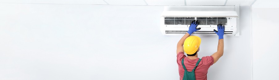 Male technician checking air conditioner indoors, space for text. Banner design
